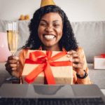 A woman wearing a party hat holds an unwrapped gift and a glass of champagne.