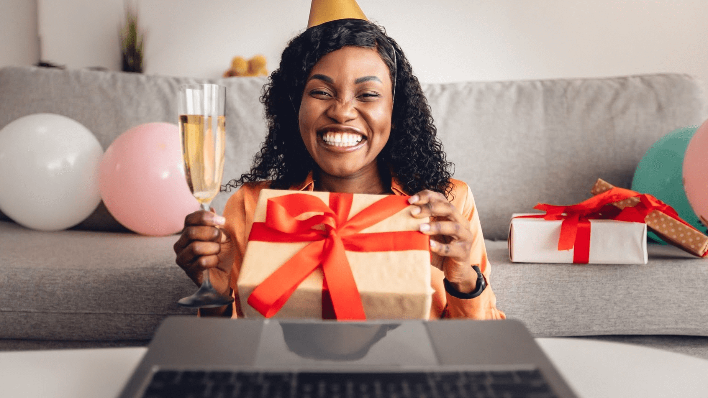 A woman wearing a party hat holds an unwrapped gift and a glass of champagne.