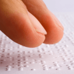 Finger tips on a sheet of Braille