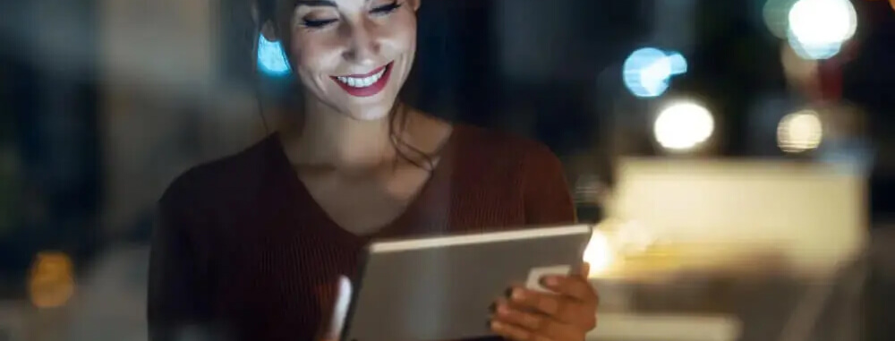 A woman happily using a tablet computer at night.