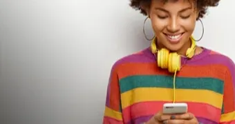 A woman wearing headphones and a vibrant sweater is focused in her phone.